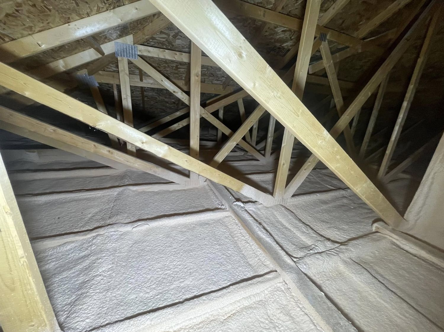 Attic floor sealed with a continuous layer of spray foam beneath open roof trusses