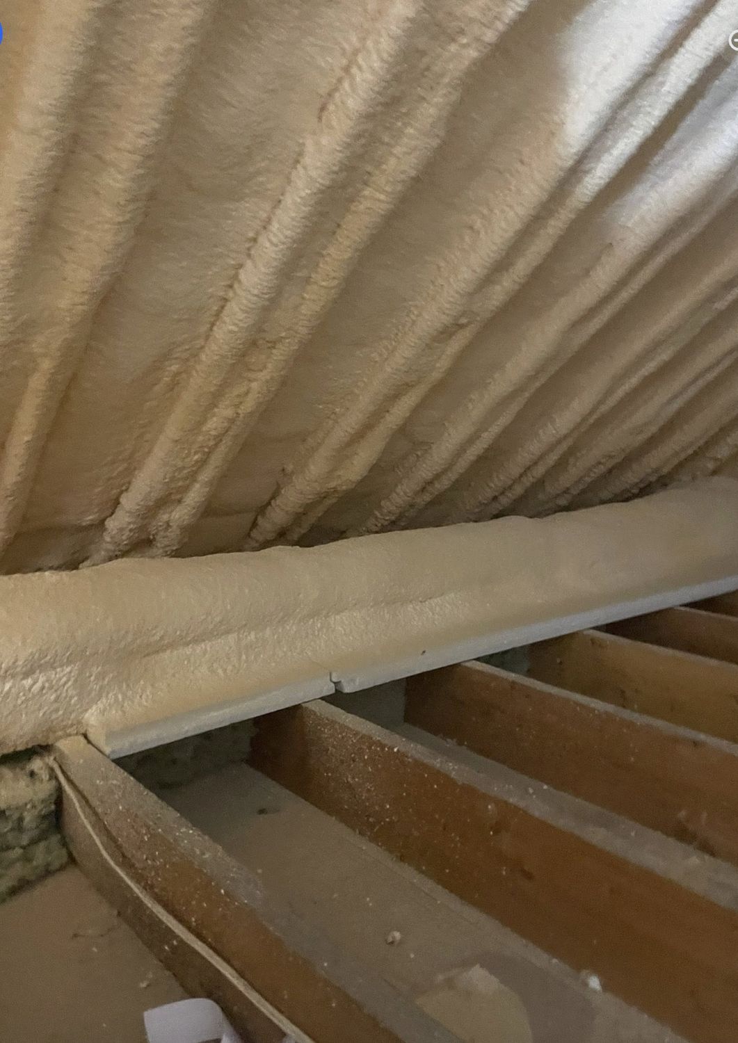 Thick spray foam covering the underside of an attic roof deck, insulated floor joists below
