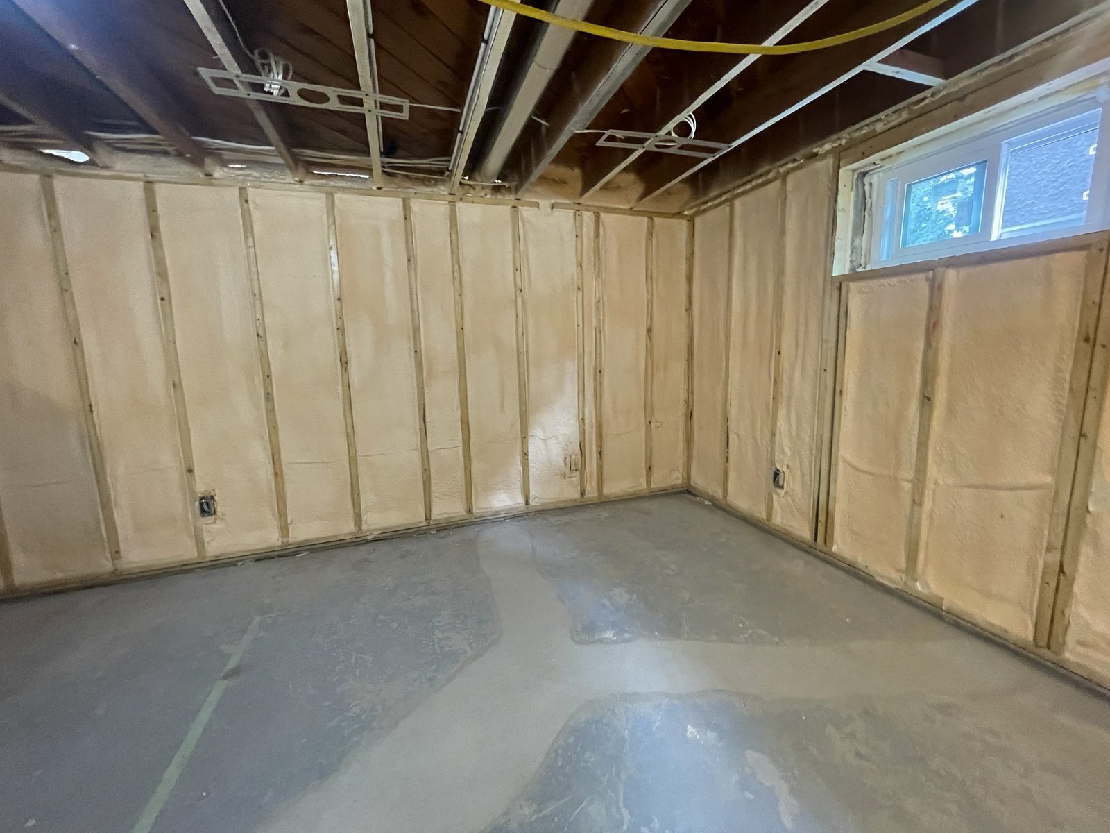 Basement room fully insulated with spray foam on walls and ceiling, ready for framing