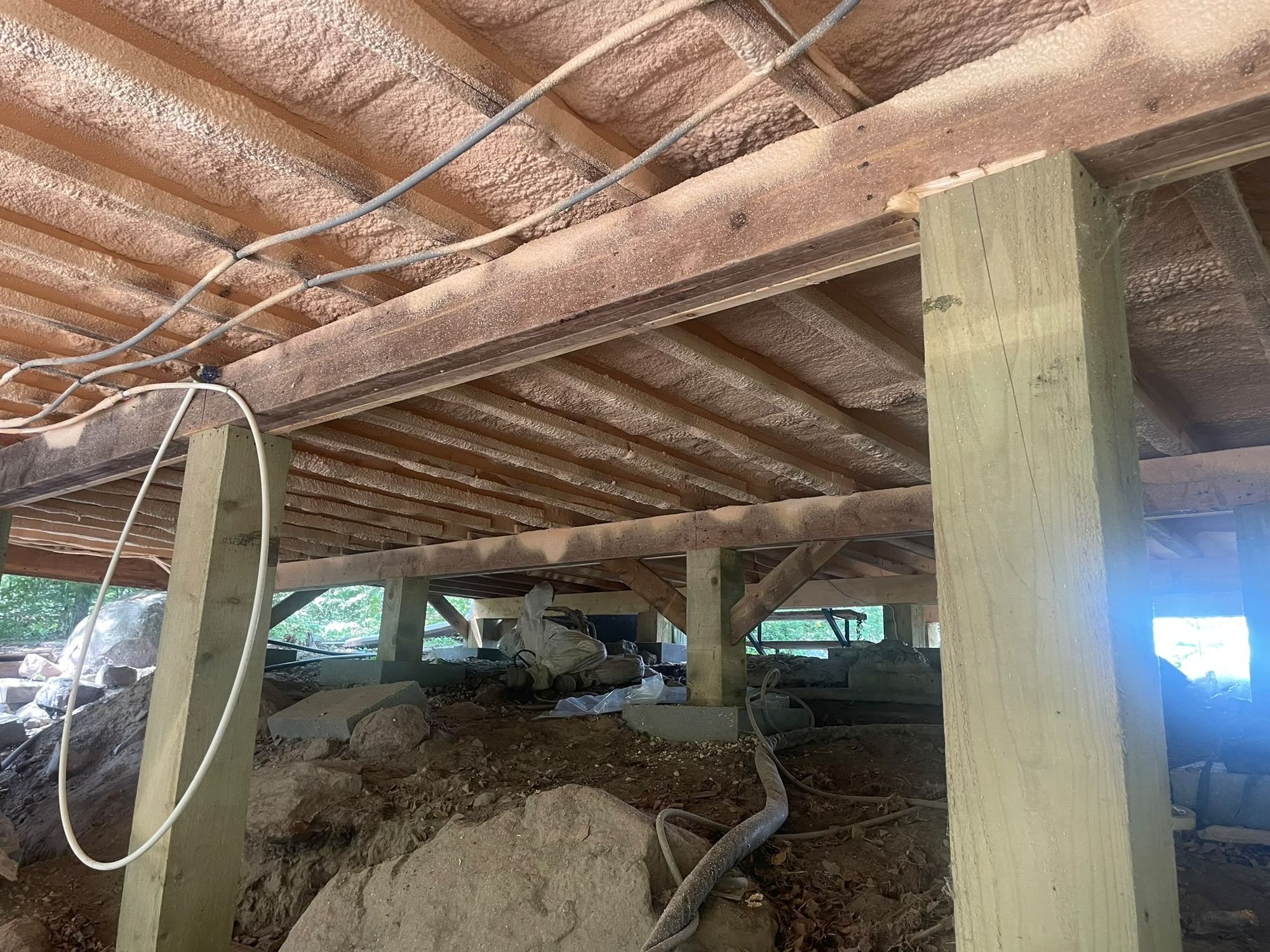 Small gable-roofed bunkie under construction with closed-cell spray foam being applied to the exterior walls from a scaffold platform