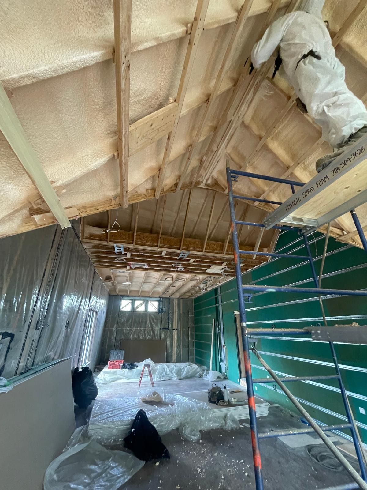 Ecologic installer in coveralls on a ladder spraying closed-cell foam into a complex dormer roofline