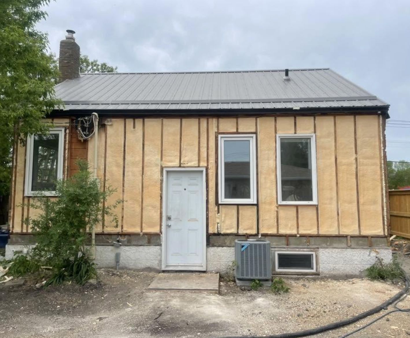 Rear of a small house with exterior walls fully covered in spray foam between strapping, under a metal roof
