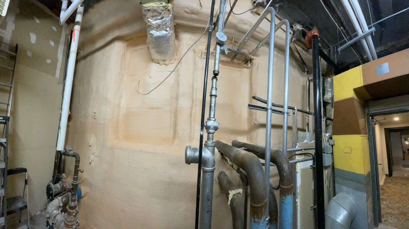 Mechanical room with multiple pipe penetrations sealed and insulated with spray foam